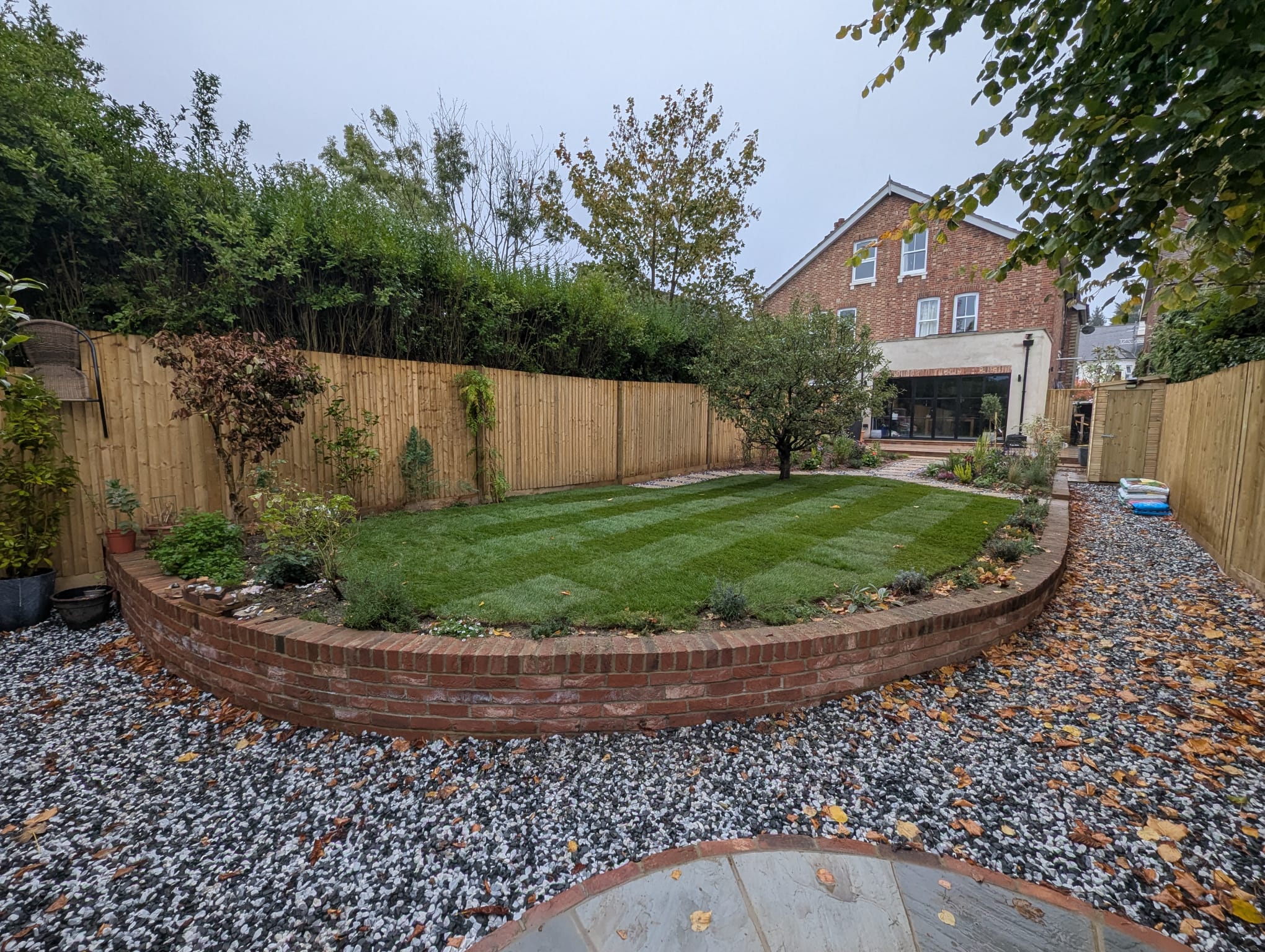 Curved brick retaining wall with slate chippings, new turf and closeboard fencing