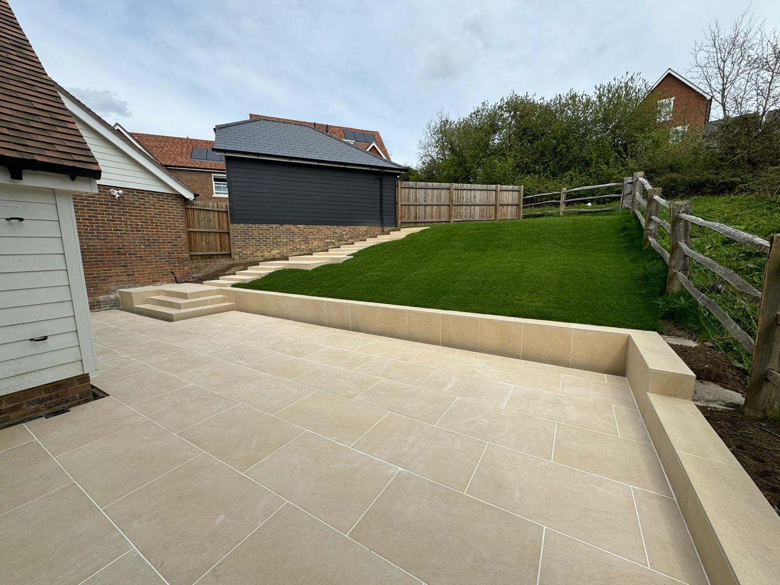 Light porcelain terrace with matching steps and retaining wall leading to a landscaped lawn